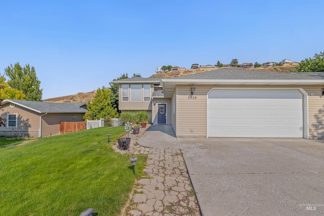 view of front facade with a front yard, concrete driveway, fence, and an attached garage