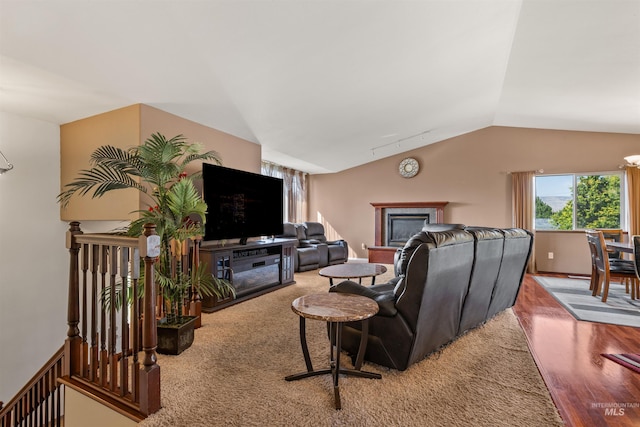 living area featuring a glass covered fireplace, carpet flooring, vaulted ceiling, and a notable chandelier