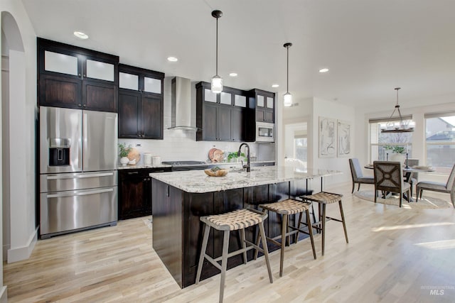 kitchen featuring dark brown cabinets, wall chimney range hood, a center island with sink, and stainless steel appliances