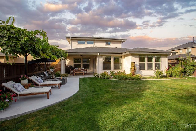 back house at dusk featuring ceiling fan, a patio area, and a lawn