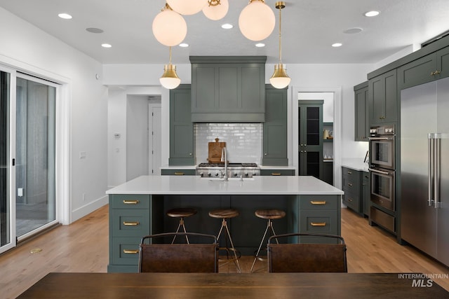 kitchen with pendant lighting, stainless steel appliances, light hardwood / wood-style floors, and a kitchen island with sink