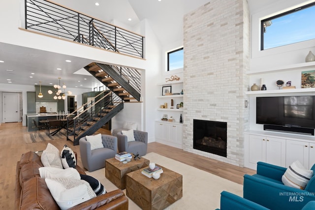 living room featuring a fireplace, light hardwood / wood-style floors, a notable chandelier, built in features, and a towering ceiling