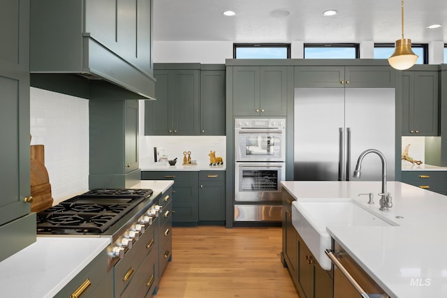 kitchen featuring tasteful backsplash, sink, hanging light fixtures, appliances with stainless steel finishes, and light hardwood / wood-style floors