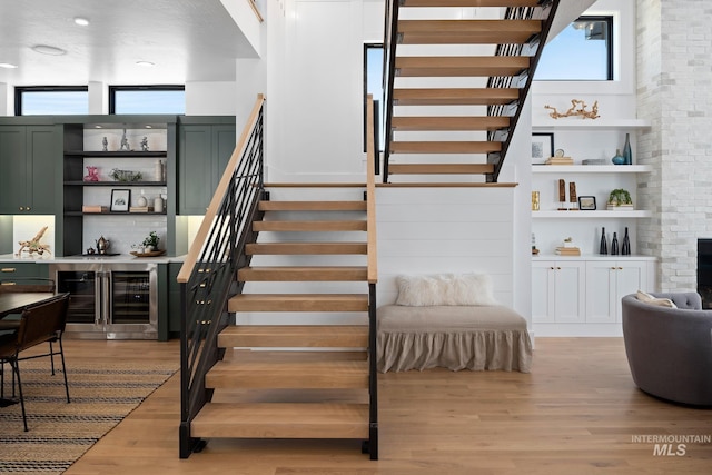 stairway featuring a fireplace, hardwood / wood-style flooring, a towering ceiling, and beverage cooler