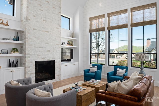 living room with built in shelves, a large fireplace, a towering ceiling, and light hardwood / wood-style flooring