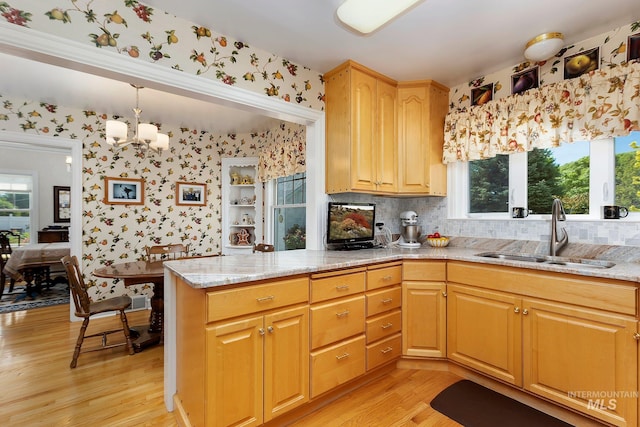 kitchen with decorative light fixtures, sink, a chandelier, light hardwood / wood-style floors, and kitchen peninsula