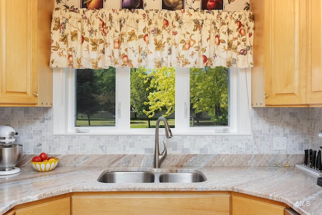 kitchen with light brown cabinetry, sink, backsplash, and light stone counters