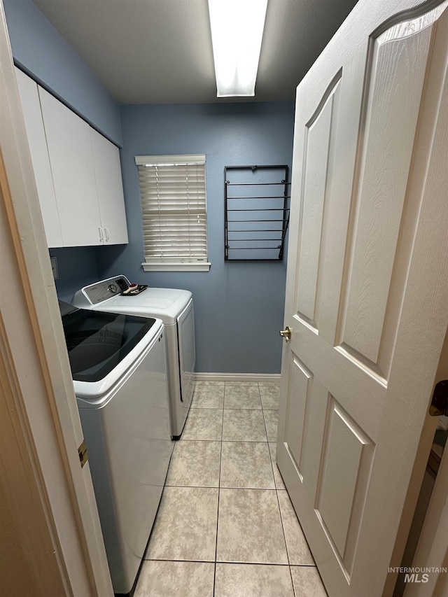 clothes washing area with washing machine and clothes dryer, baseboards, light tile patterned flooring, and cabinet space