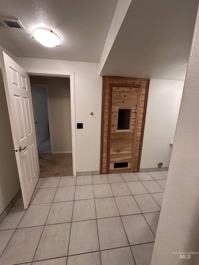 hallway with baseboards, visible vents, a textured ceiling, and light tile patterned floors