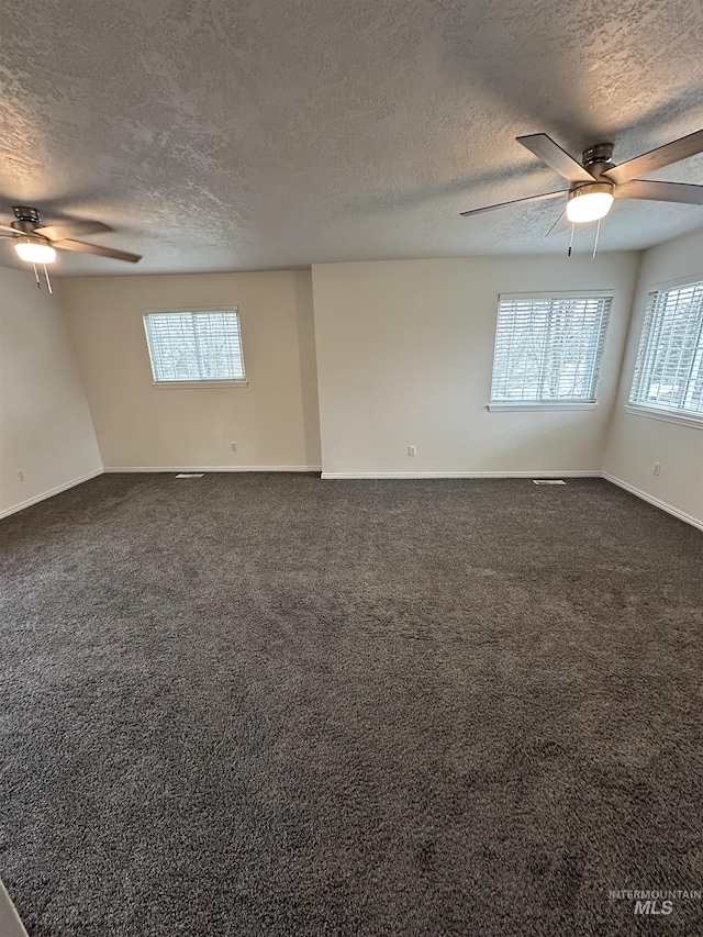 empty room featuring dark carpet, a ceiling fan, baseboards, and a textured ceiling
