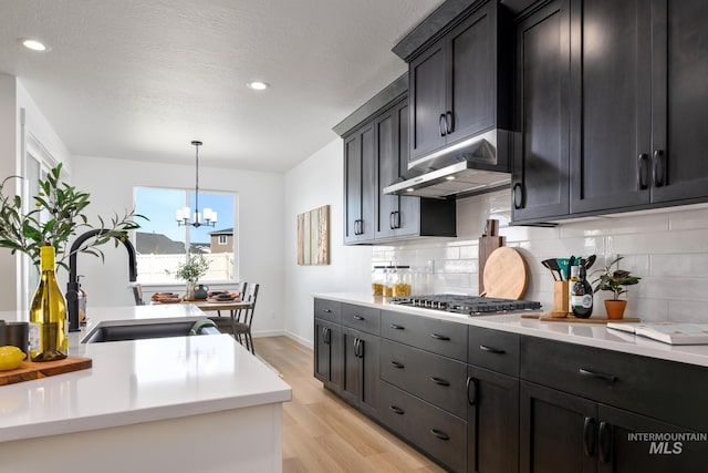 kitchen featuring backsplash, stainless steel gas stovetop, under cabinet range hood, and light wood-type flooring