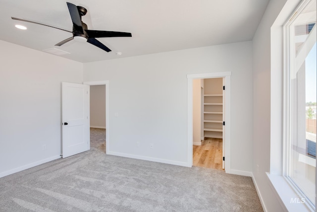 unfurnished bedroom featuring ceiling fan, a walk in closet, and light carpet