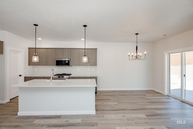 kitchen with sink, decorative light fixtures, stainless steel appliances, and an island with sink