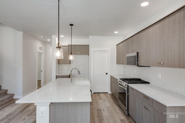 kitchen with stainless steel appliances, pendant lighting, a center island with sink, and light wood-type flooring