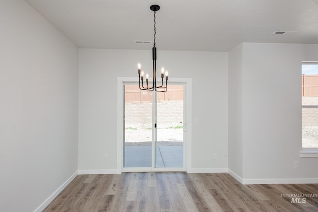 unfurnished dining area with a wealth of natural light, a notable chandelier, and light hardwood / wood-style flooring