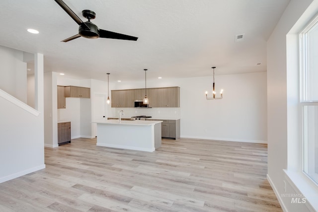 kitchen with backsplash, decorative light fixtures, light hardwood / wood-style flooring, and a center island with sink