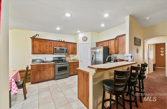 1207 Empire Ct, Caldwell, ID 83607 - kitchen featuring appliances with stainless steel finishes, arched walkways, a peninsula, brown cabinets, and a breakfast bar