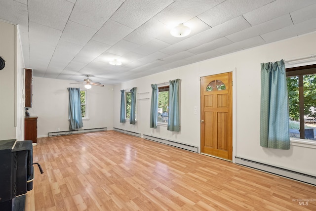 unfurnished living room with a baseboard heating unit, light wood-style flooring, a ceiling fan, and a wood stove