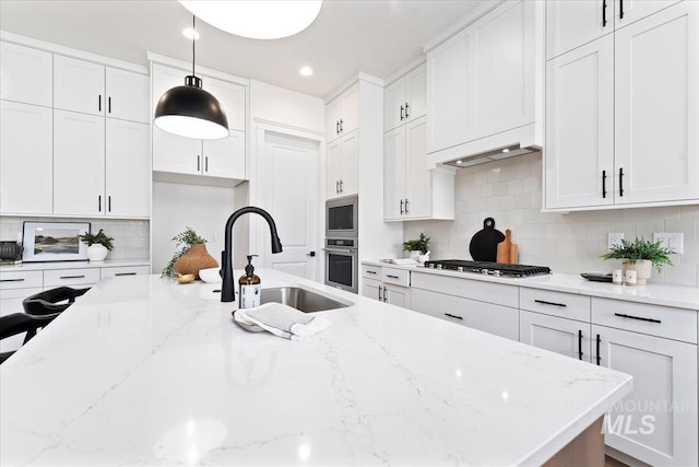 kitchen featuring sink, light stone counters, pendant lighting, white cabinets, and appliances with stainless steel finishes