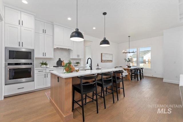 kitchen featuring white cabinets, pendant lighting, stainless steel appliances, and a center island with sink