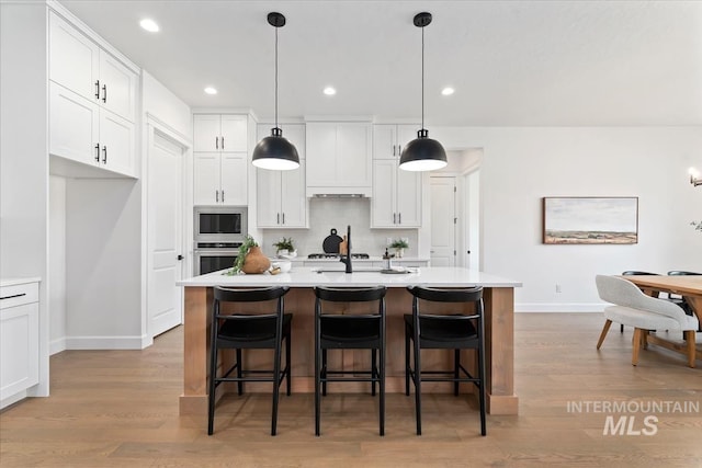 kitchen with pendant lighting, white cabinets, and a kitchen island with sink