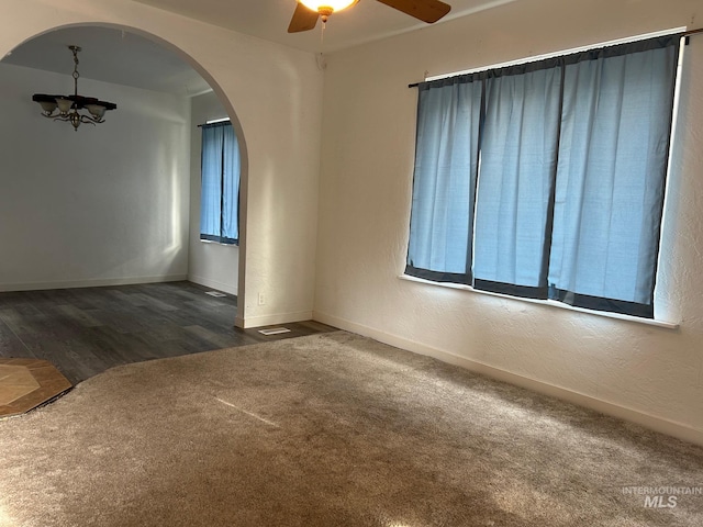 empty room with dark colored carpet and ceiling fan with notable chandelier