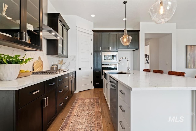kitchen featuring glass insert cabinets, decorative backsplash, stainless steel appliances, a sink, and wood finished floors