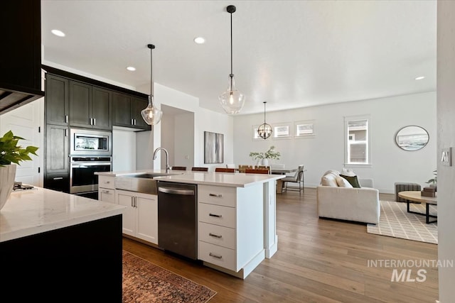 kitchen featuring recessed lighting, appliances with stainless steel finishes, wood finished floors, a sink, and open floor plan