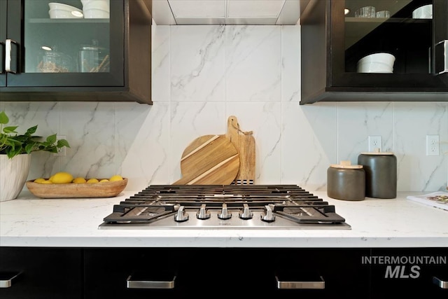 room details featuring stainless steel gas cooktop, light stone counters, backsplash, and glass insert cabinets