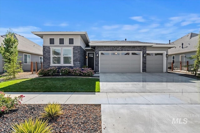 prairie-style home with concrete driveway, stone siding, a front lawn, a garage, and fence