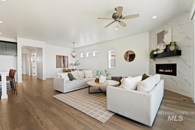 living room with recessed lighting, ceiling fan with notable chandelier, wood finished floors, and a premium fireplace