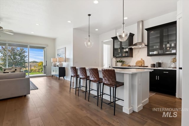 kitchen featuring tasteful backsplash, wall chimney range hood, open floor plan, a breakfast bar, and light countertops