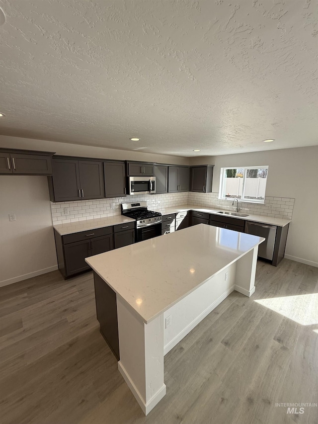 kitchen with appliances with stainless steel finishes, light wood-type flooring, a sink, and decorative backsplash