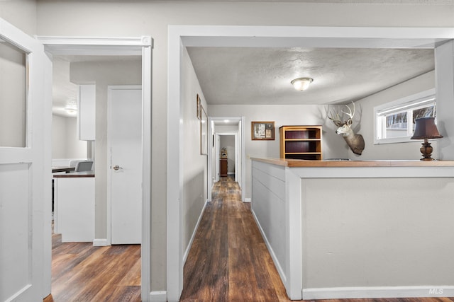 hallway featuring a textured ceiling, wood finished floors, and baseboards