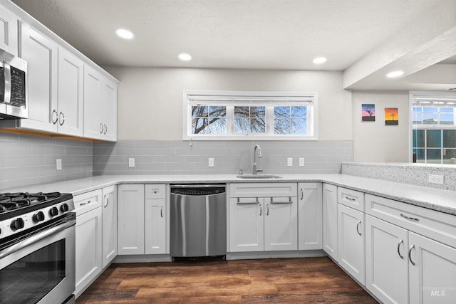 kitchen featuring appliances with stainless steel finishes, dark wood-type flooring, a sink, and decorative backsplash