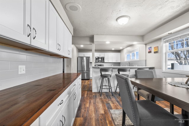 kitchen with stainless steel appliances, a breakfast bar, white cabinetry, wooden counters, and dark wood finished floors