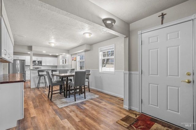 dining area with a wainscoted wall, a textured ceiling, and wood finished floors