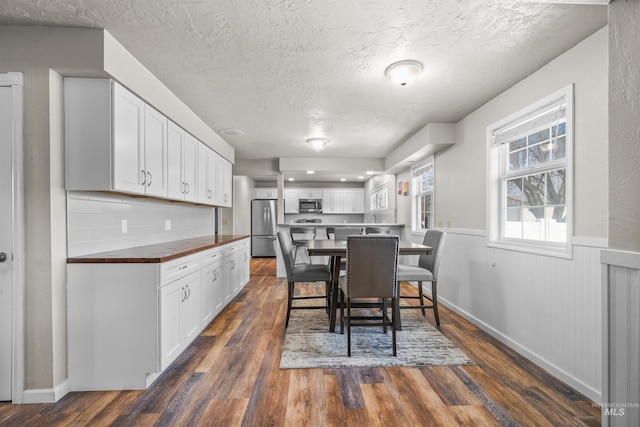 dining room with a wainscoted wall, dark wood-style flooring, and a textured ceiling