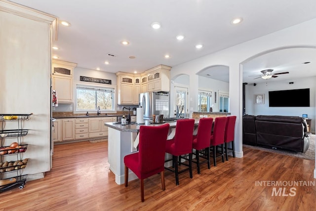 kitchen with stainless steel refrigerator with ice dispenser, a breakfast bar, cream cabinets, and light wood-type flooring