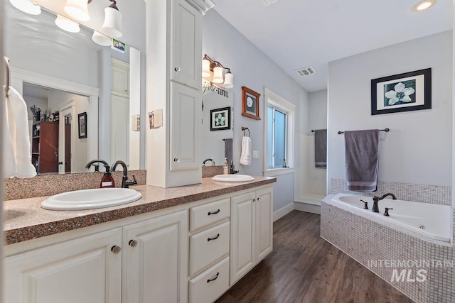 bathroom with vanity, wood-type flooring, and a relaxing tiled tub