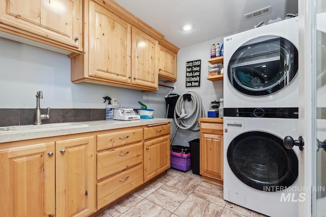 clothes washing area with sink, cabinets, and stacked washer and clothes dryer