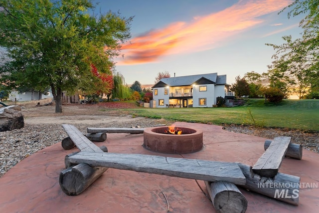 patio terrace at dusk featuring a balcony, a lawn, and a fire pit