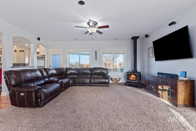 living room with carpet, a wood stove, and ceiling fan