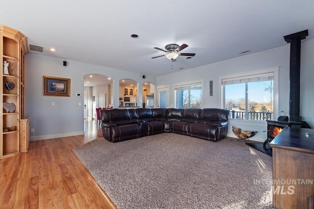 living room with ceiling fan, light hardwood / wood-style flooring, and a wood stove