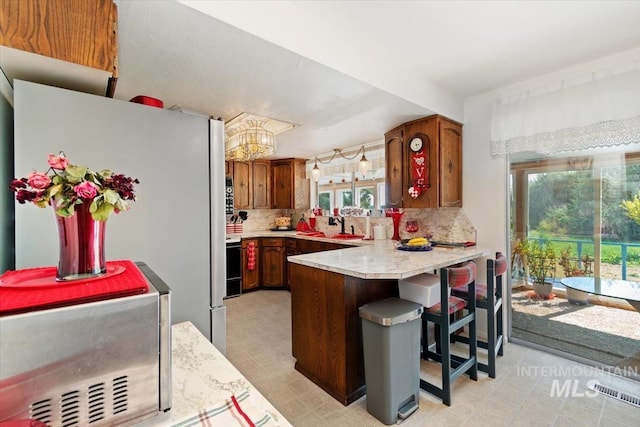 23743 Viking Ln, Wilder, ID 83676 - kitchen featuring a peninsula, light countertops, decorative backsplash, a chandelier, and brown cabinets