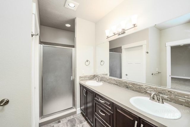 full bathroom with double vanity, backsplash, a sink, and a shower stall