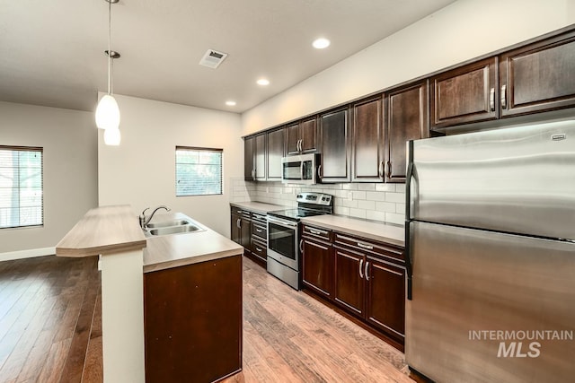 kitchen with light wood-type flooring, tasteful backsplash, stainless steel appliances, and a sink