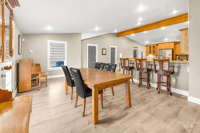 dining area with light hardwood / wood-style flooring and vaulted ceiling with beams