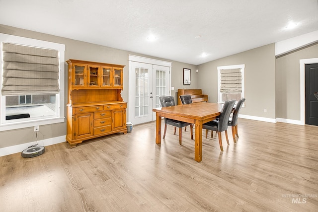 dining space with french doors, light hardwood / wood-style flooring, lofted ceiling, and a textured ceiling