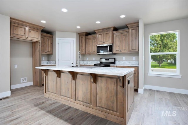 kitchen featuring a kitchen island with sink, electric stove, sink, a breakfast bar, and light hardwood / wood-style floors